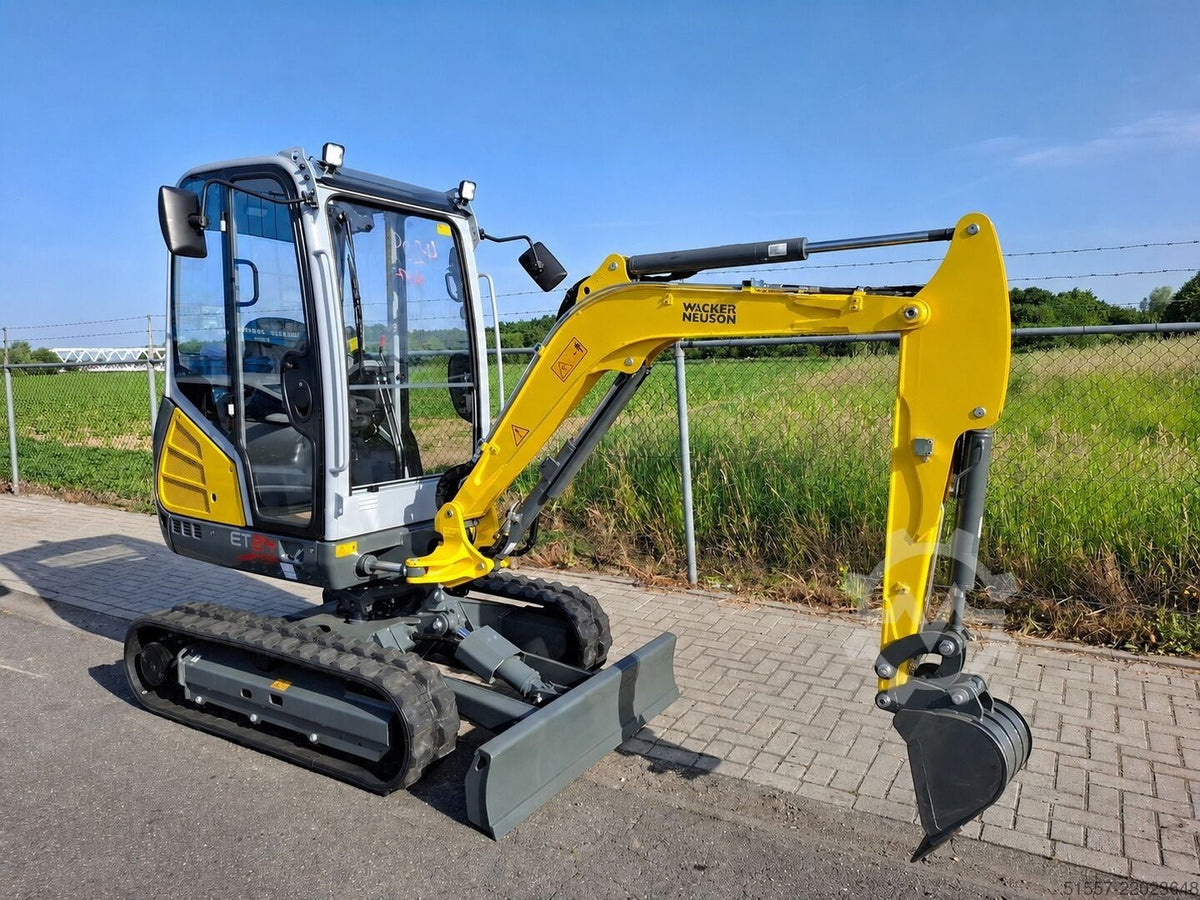 Mini pelle Ma boutique Wacker Neuson ET24 jaune et grise avec cabine vitrée et chenilles sur un chantier extérieur